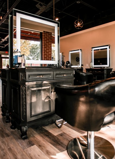 Elegant salon station at Penton House Salon & Spa featuring ornate cabinetry, a backlit mirror, and a plush black styling chair in a warm, upscale setting with wood-look flooring.
