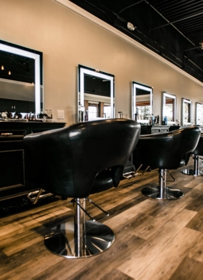 Row of modern black salon chairs facing illuminated mirrors along a stylish workstation at Sharon Daniel Salon, with woodgrain floors and a contemporary, professional atmosphere.